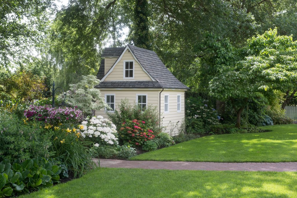 A charming playhouse sits in a shaded perennial garden.